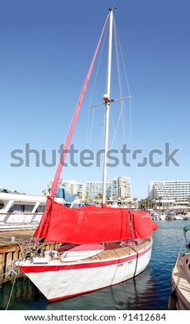 Yacht with a red sail moored in marine on the yacht club background (Eilat, Israel)