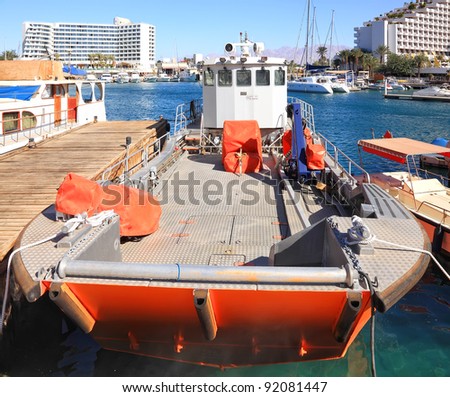 Cargo orange boat with the open deck, moored in gulf on the mountains and hotels background