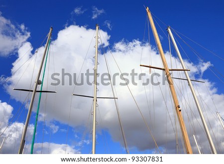Masts and a rigging of yachts on the cloudy blue sky background