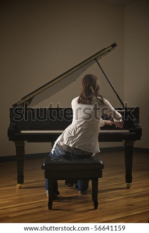 Young pretty girl playing piano in indoor concert hall