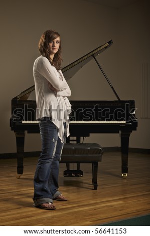 Young pretty girl standing in front of a piano in indoor concert hall
