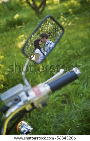 A cute couple kissing in the reflection of a motorcycle mirror