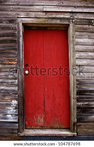 A wooden door, painted red, with a white doorknob, on a wooden building