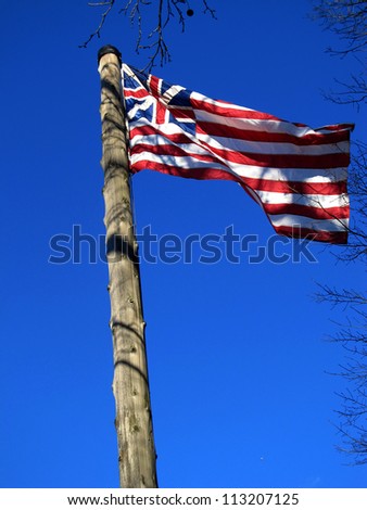 The flag of the British North American colonies flies atop a wooden flag pole.