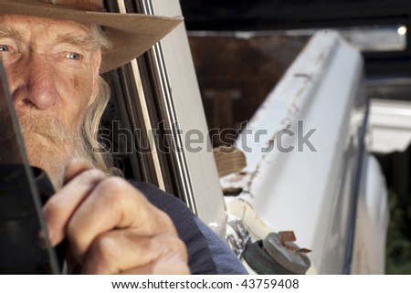 An elderly man with a white beard driving a pickup truck and staring out the window