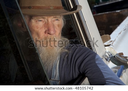 An elderly man with a white beard driving a pickup truck and staring out the window