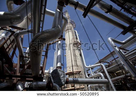 Low angle, exterior view of a tower at a gas compressor plant as seen through a variety of piping. Horizontal shot.
