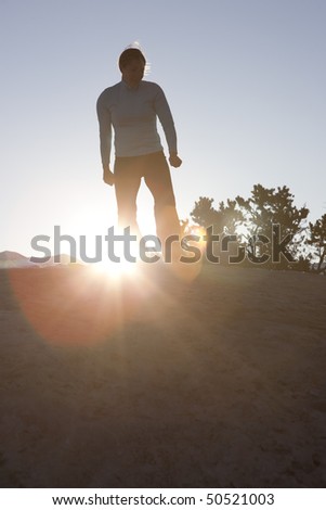 A woman is standing on a hill and looking down with the sun shining behind her. Vertical shot.