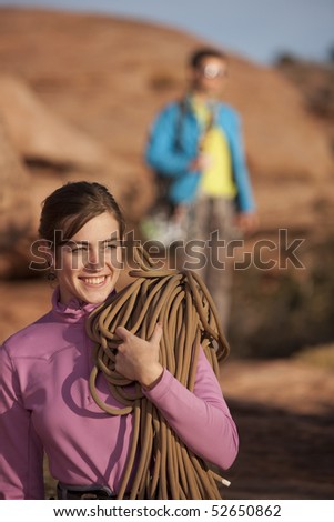 An attractive young woman is holding a rope in preparation for rock climbing. A man can be seen in the background. Vertical shot.