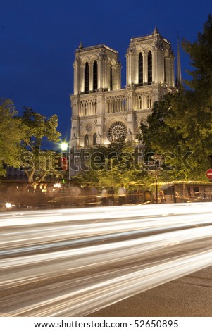 The towers of the Notre Dame Cathedral in Paris, France at night.  Lights from cars can be seen in the foreground. Vertical shot.