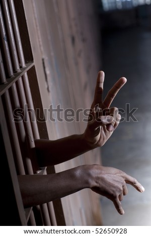 A man gestures the peace sign while sticking his hands through the bars of his prison cell. Vertical shot.