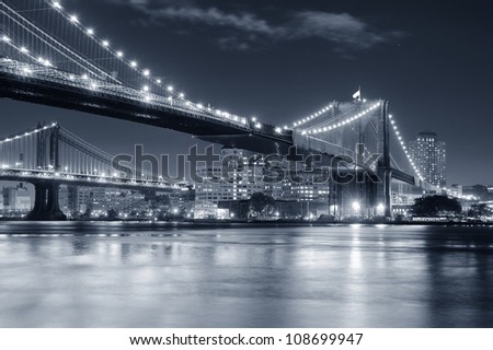 Brooklyn Bridge over East River at night in black and white in New York City Manhattan with lights and reflections.