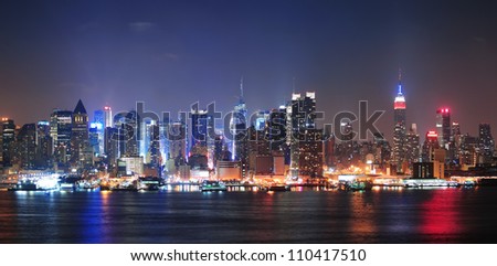 New York City Manhattan midtown skyline at night with skyscrapers lit over Hudson River with reflections.