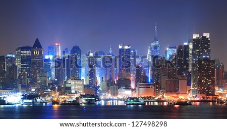 New York City Manhattan midtown skyline at night with skyscrapers lit over Hudson River with reflections.