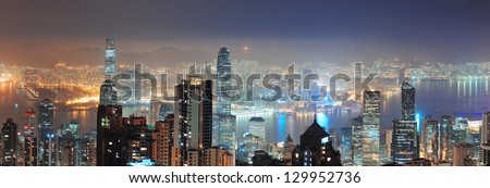 Hong Kong city skyline panorama at night with Victoria Harbor and skyscrapers illuminated by lights over water viewed from mountain top.