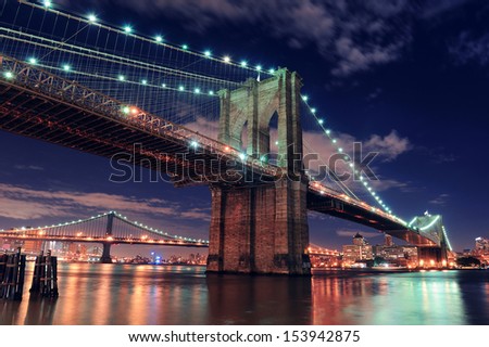 Brooklyn Bridge Closeup Over East River At Night In New York City Manhattan With Lights And Reflections.
