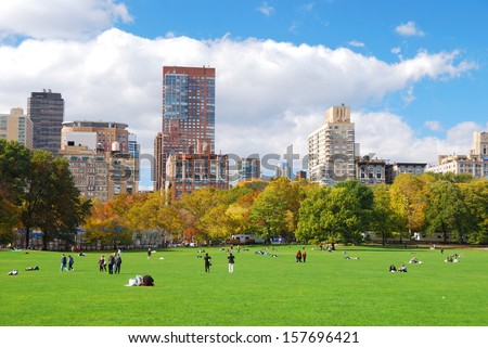 New York City Manhattan skyline panorama viewed from Central Park with cloud and blue sky and people in lawn.