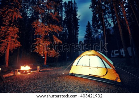 Camping in forest with tent light and bonfire in Banff National Park