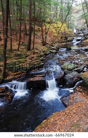 Autumn creek with hiking trail and rocks in woods with colorful foliage.