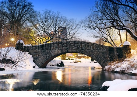 New York City Manhattan Central Park in winter with bridge over lake with snow, ducks and light at dusk.