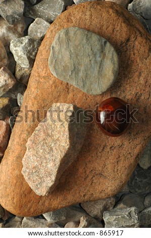 Arrangement of three different kinds of rock on a larger rock on a bed of gravel