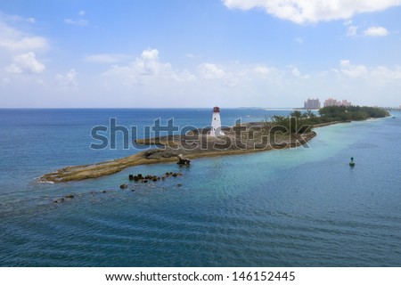 White Lighthouse on an island surrounded by a deep blue and aqua ocean with a large resort on the horizon