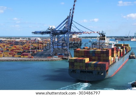 Port of Freeport Bahamas Container shipyard with heavy lifting Cranes and a ship coming in to dock assisted by tug boats