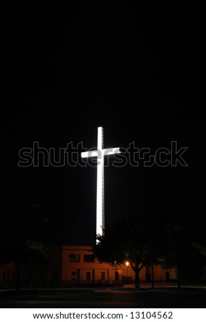 Religious cross lit up at night over a church with floodlights
