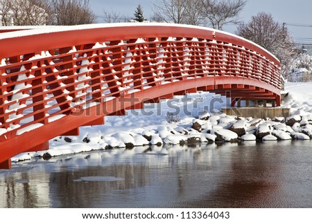 A pedestrian bridge spans a small span of water in the winter landscape.