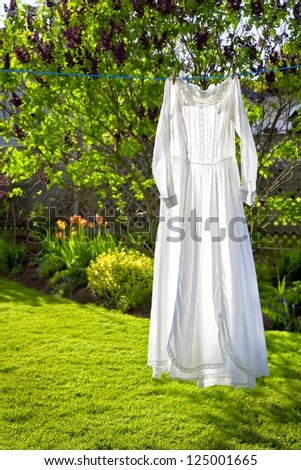 A white lacey vintage dress hanging on a cloths line with strong backlighting.