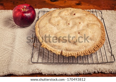 Homemade apple pie cooling on a wire baking rack and sitting beside a cortland apple.