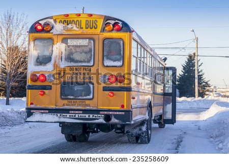 A typical yellow school bus stopped to pick up passengers on an extremely cold winter day.