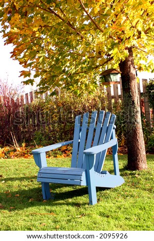 A blue lawn chair sitting out under a maple tree with its golden fall foliage.