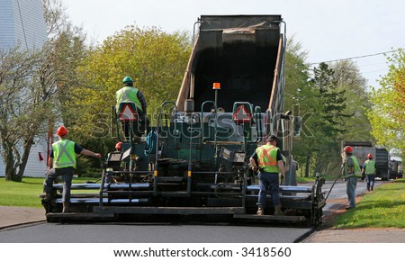 Paving a residential street by laying asphalt which is initially in the dump truck and then is \'pressed\' down to form the new road surface.