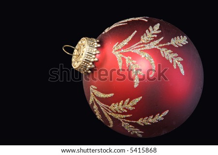 A red Christmas ball with a matte finish and gold leaf-like drawings.  All against a black background.