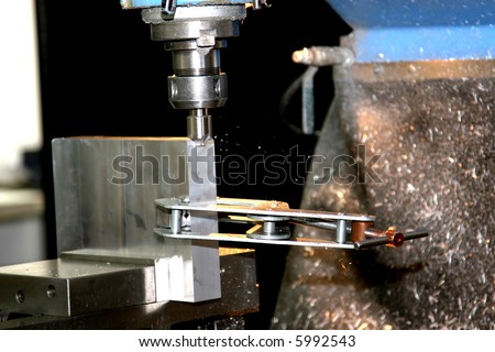 A computerized machine making precision cuts in metal pieces while the small metal pieces are flung violently from the work.