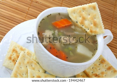 A cup of healthy homemade chicken vegetable soup with crackers and a spoon.