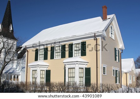 An old style home next to  a church steeple, in winter.