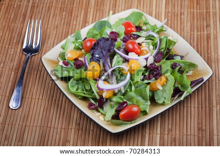 A plate of California salad containing oranges, dried cranberries, red onion, mixed lettuce, sliced almond and minitaure tomatoes.