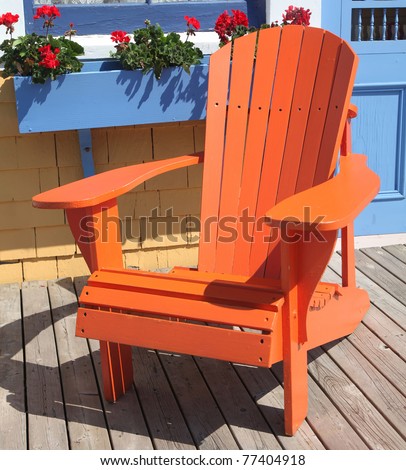 Colorful Adirondack chair sitting on a patio or deck with a window box full of geraniums.