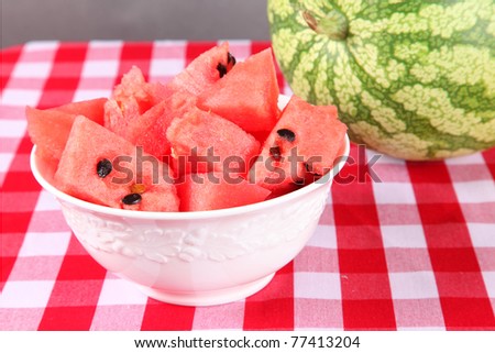 Pieces of fresh cut up watermelon in a white bowl on a gingham table cloth