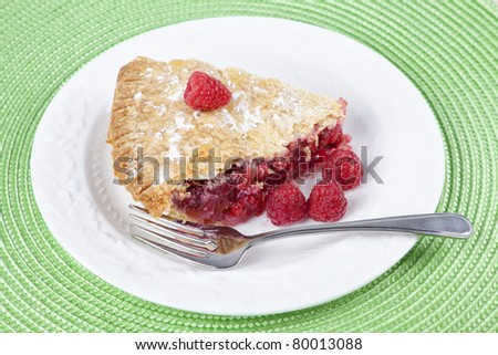 Homemade raspberry pie with fresh ripe raspberries on a white porcelain plate.
