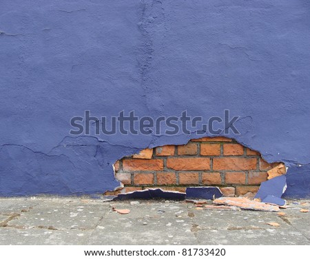 sidewalk with blue damaged wall showing bricks