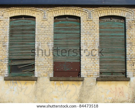 detail of 3 windows with roller shutter in  abandoned industrial building wall