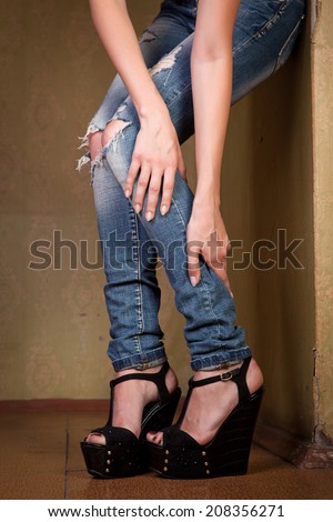 Female legs in torn jeans and shoes near the old wall.