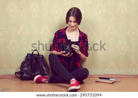 Old vintage film camera in the hands of a young girl in a red plaid shirt sitting near the old yellow wall.