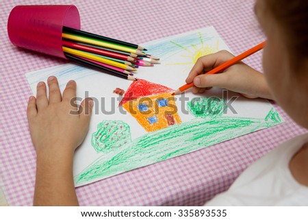Child draws a pencil drawing of the peace. Green field, the bushes and the house.