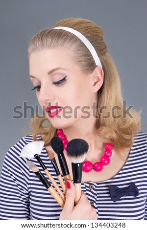 dreaming pinup woman with make up brushes over grey