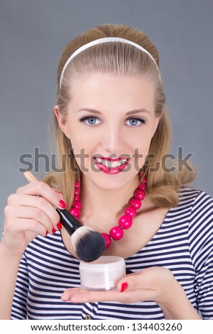 portrait of young pinup woman with make up brush and powder over grey