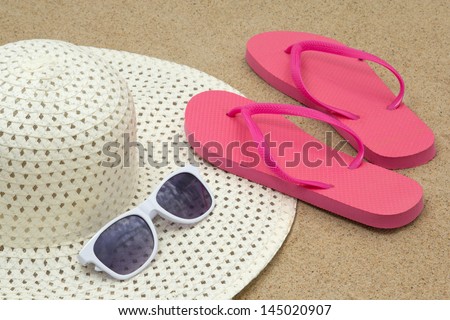 picture of pink flip flops, sunglasses and hat on white beach sand